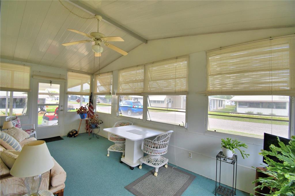 A sunroom with teal carpeting, a ceiling fan, white furniture, and large windows with blinds — 6773 BRENTWOOD DRIVE NE, WINTER HAVEN, FL