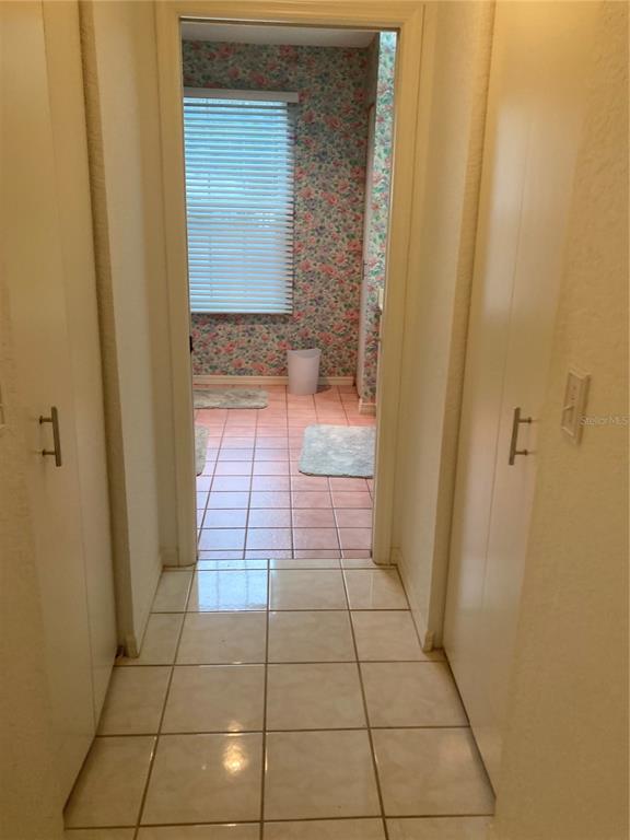 A hallway with white cabinets leads to a bathroom featuring floral wallpaper and tiled floors — 8744 SW 108TH LANE ROAD, OCALA, FL
