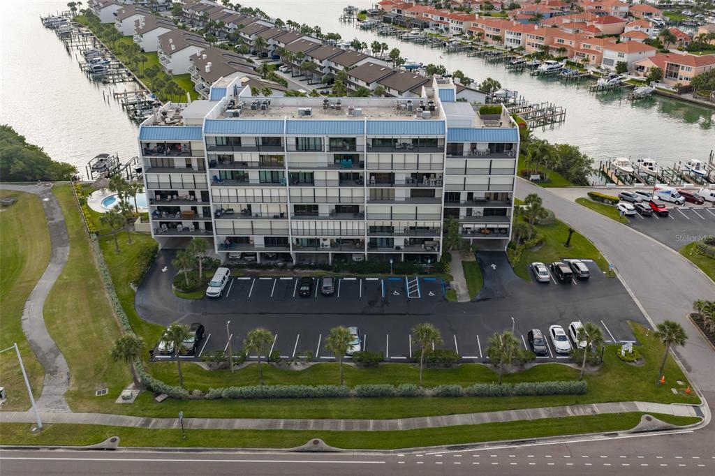 An aerial view shows a multi-story apartment building with a parking lot and waterfront docks — 1581 GULF BOULEVARD UNIT 103N, CLEARWATER BEACH, FL