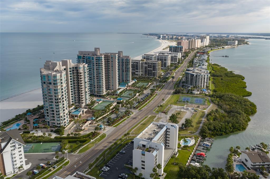 An aerial view shows high-rise condominiums along a beach with a road and mangroves nearby — 1581 GULF BOULEVARD UNIT 103N, CLEARWATER BEACH, FL