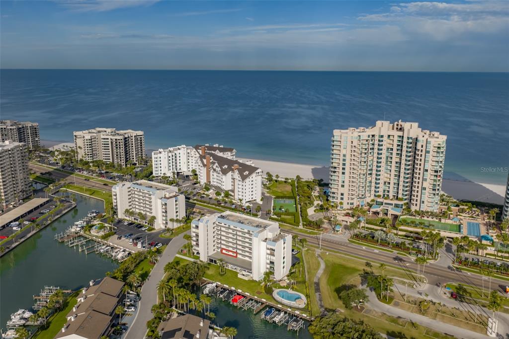 An aerial view shows several waterfront condominium buildings, a marina, and a sandy beach — 1581 GULF BOULEVARD UNIT 103N, CLEARWATER BEACH, FL