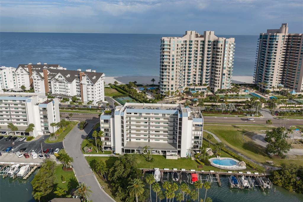 An aerial view shows multiple waterfront condominium buildings, a swimming pool, and boat docks — 1581 GULF BOULEVARD UNIT 103N, CLEARWATER BEACH, FL