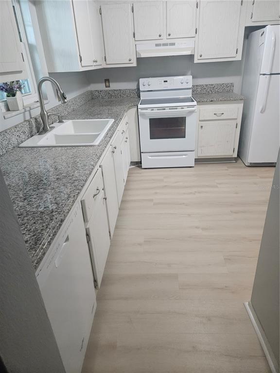 A kitchen featuring white cabinets, granite countertops, a white stove, and light wood-look flooring — 1706 BELLEAIR FOREST DRIVE UNIT 310, CLEARWATER, FL
