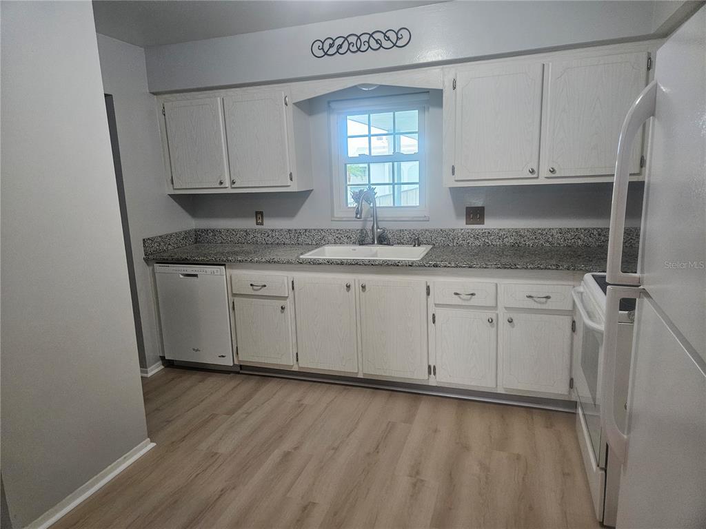 A kitchen features white cabinets, granite countertops, a white sink, and light wood-look flooring — 1706 BELLEAIR FOREST DRIVE UNIT 310, CLEARWATER, FL