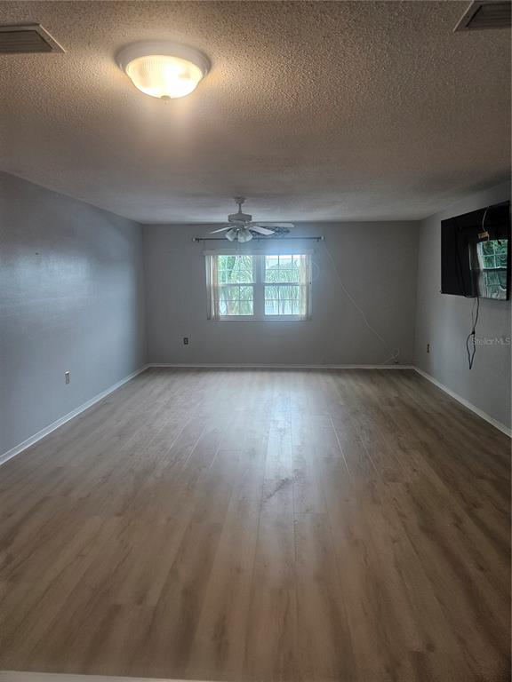 An empty living room features light wood-look flooring, gray walls, a ceiling fan, and a window — 1706 BELLEAIR FOREST DRIVE UNIT 310, CLEARWATER, FL