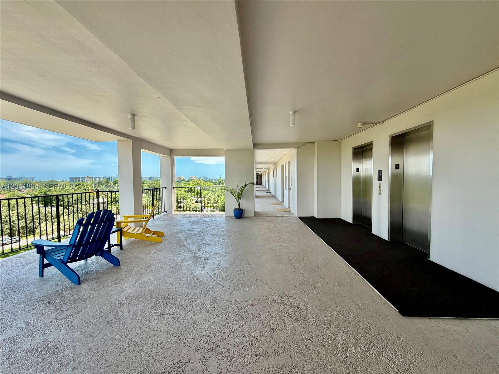 An outdoor hallway features two elevators, a concrete floor, and two chairs overlooking trees — 3200 N Palm Aire Dr # 710, Pompano Beach FL 33069, POMPANO BEACH, FL