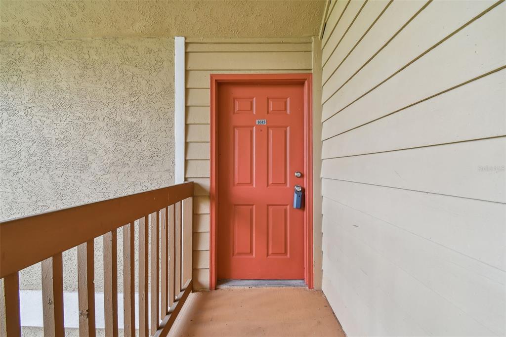 An exterior view of an orange apartment door with a lockbox on a balcony — 9481 HIGHLAND OAK DRIVE UNIT 1615, TAMPA, FL