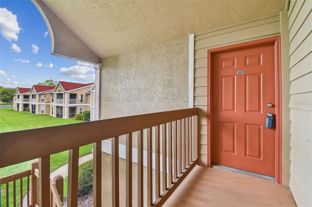 An orange apartment door with a number plate sits on a covered outdoor balcony — 9481 HIGHLAND OAK DRIVE UNIT 1615, TAMPA, FL