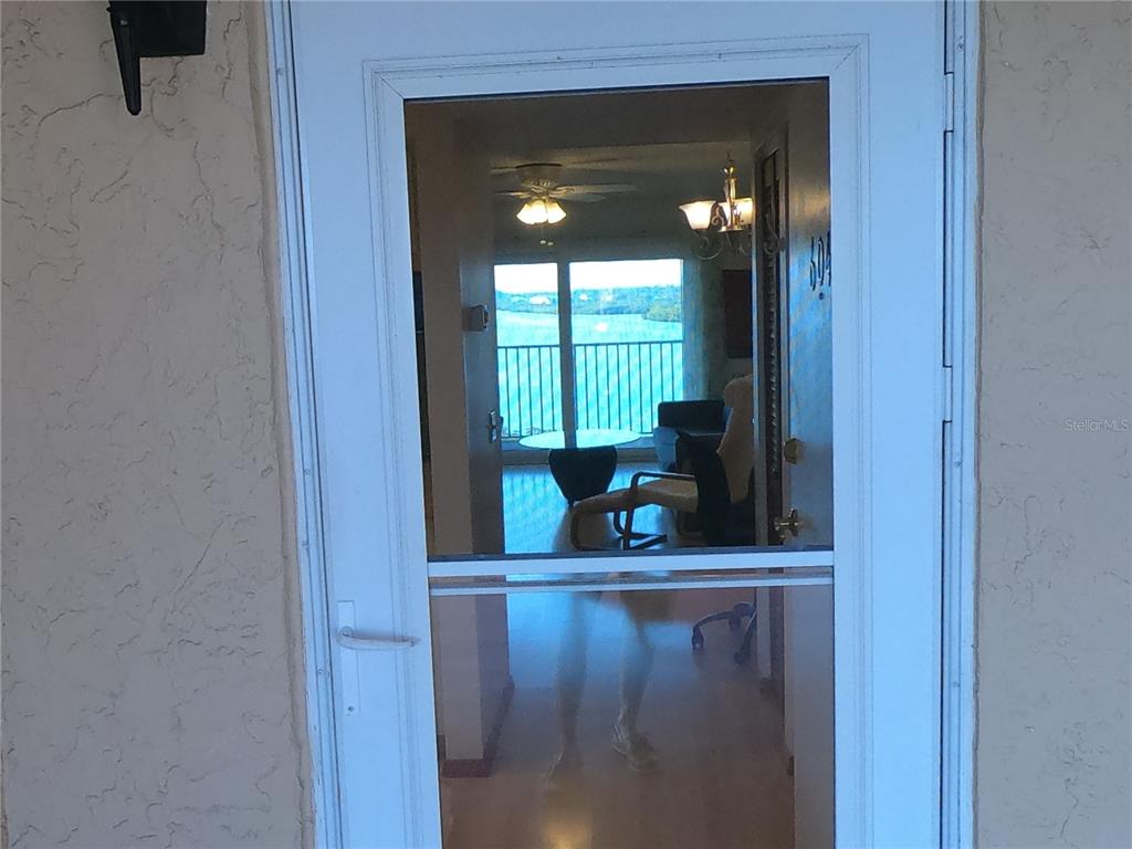A white storm door provides a view into a living area with a balcony overlooking water — 19451 GULF BOULEVARD UNIT 604, INDIAN SHORES, FL