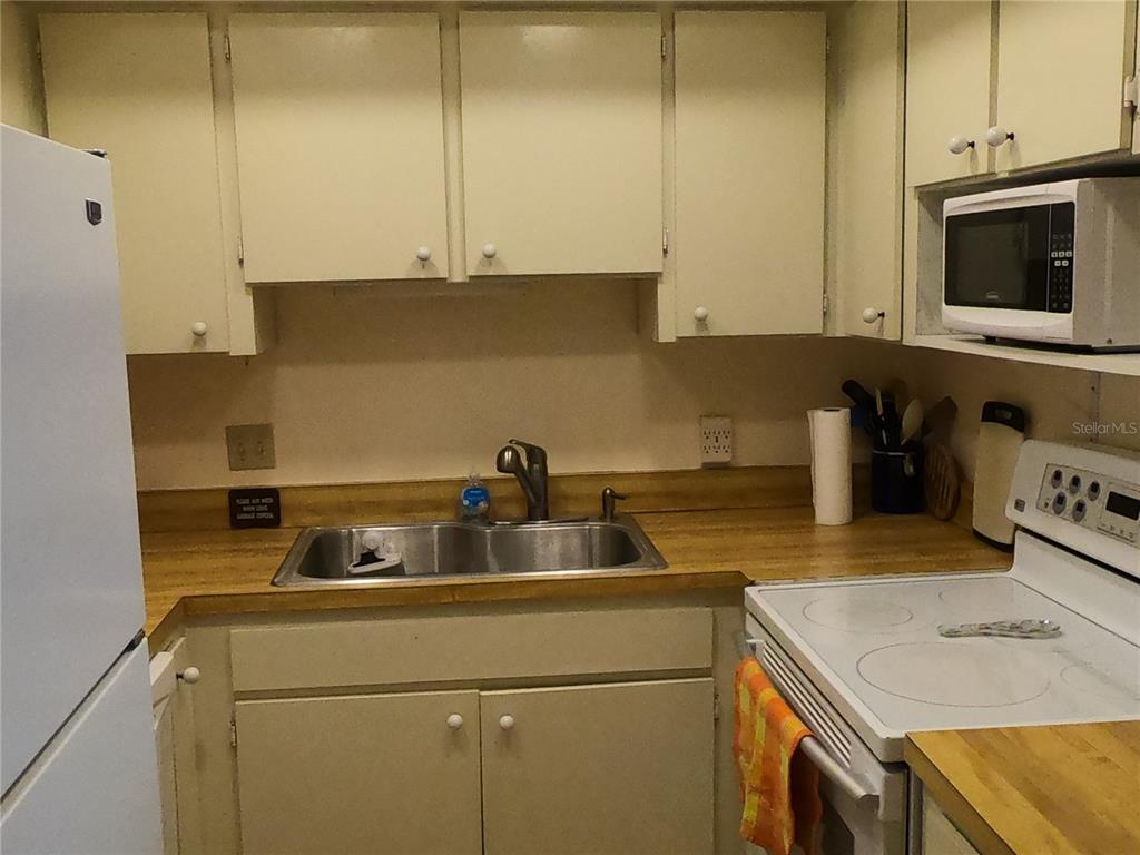 A kitchen features light-colored cabinets, a double-basin stainless steel sink, and a white electric stove — 19451 GULF BOULEVARD UNIT 604, INDIAN SHORES, FL