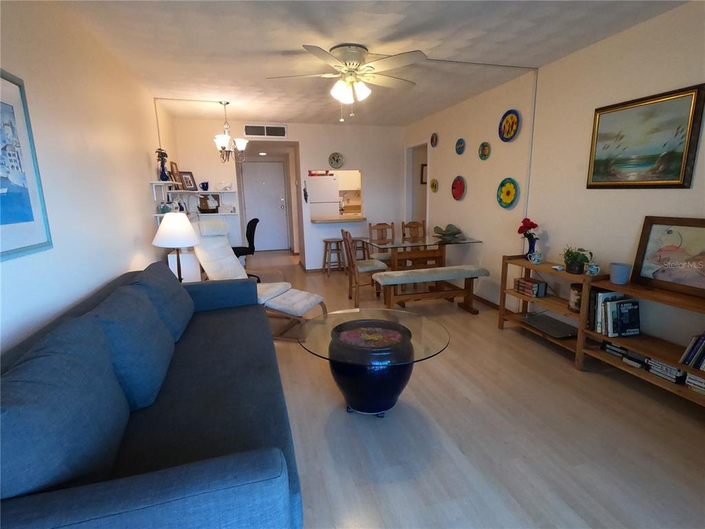 A living room with a blue sofa, glass coffee table, dining area, and light wood flooring — 19451 GULF BOULEVARD UNIT 604, INDIAN SHORES, FL