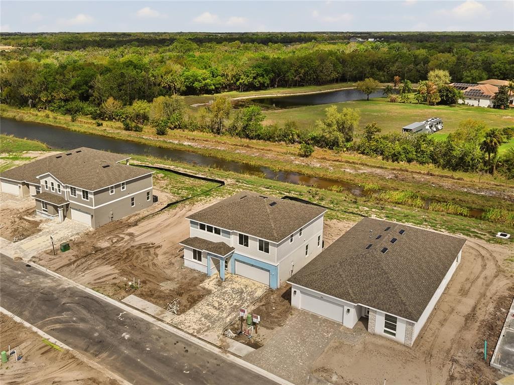 An aerial view shows three newly constructed suburban houses near a canal and pond — 14530 BANKS COURT, PARRISH, FL