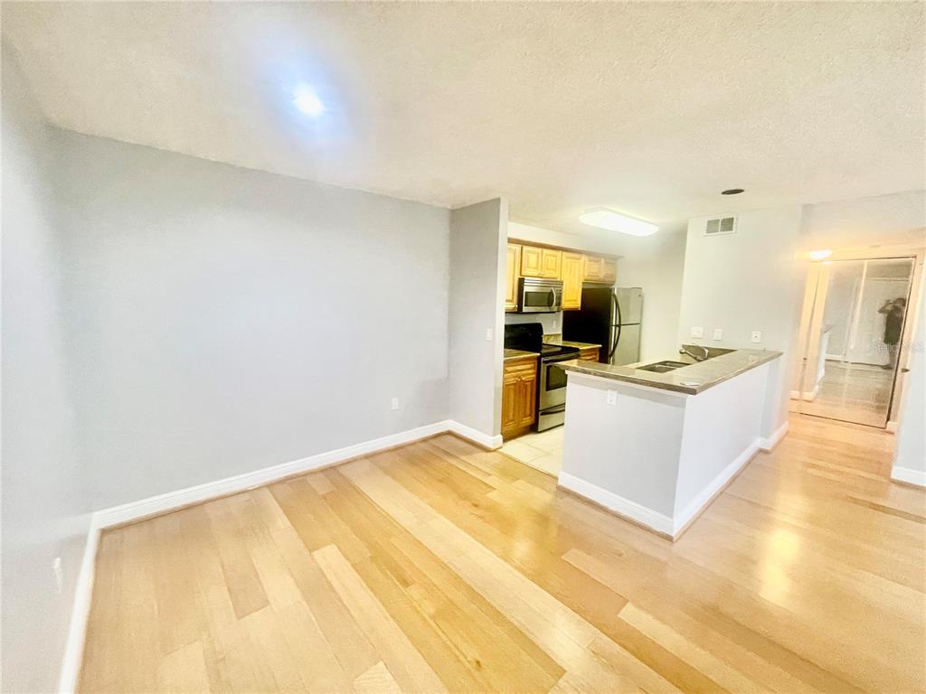 An open-concept kitchen with wood cabinets and a breakfast bar overlooks a hardwood-floored living area — 4211 CHATHAM OAK COURT UNIT 111, TAMPA, FL