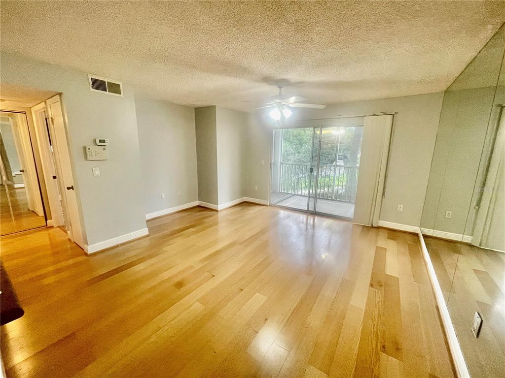 An empty living room features light wood flooring, a ceiling fan, and a sliding glass door — 4211 CHATHAM OAK COURT UNIT 111, TAMPA, FL
