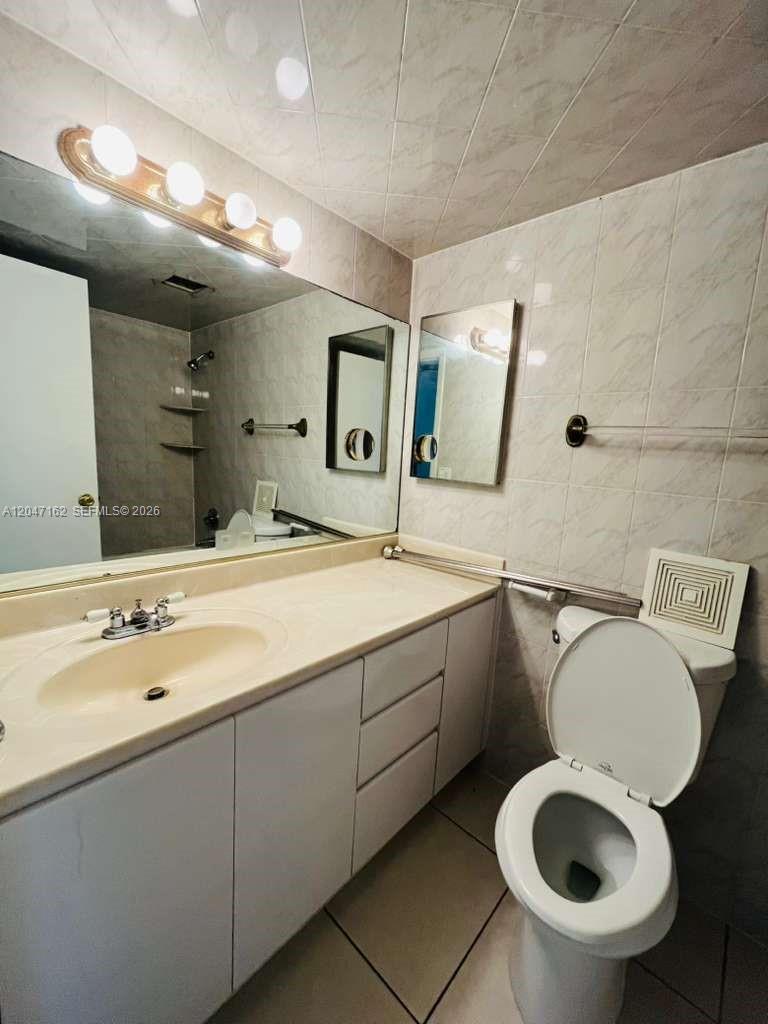 A bathroom features a vanity with a beige countertop, a large mirror, and tiled walls — 724 NE 4th St # 9, Hallandale Beach FL 33009, HALLANDALE BEACH, FL