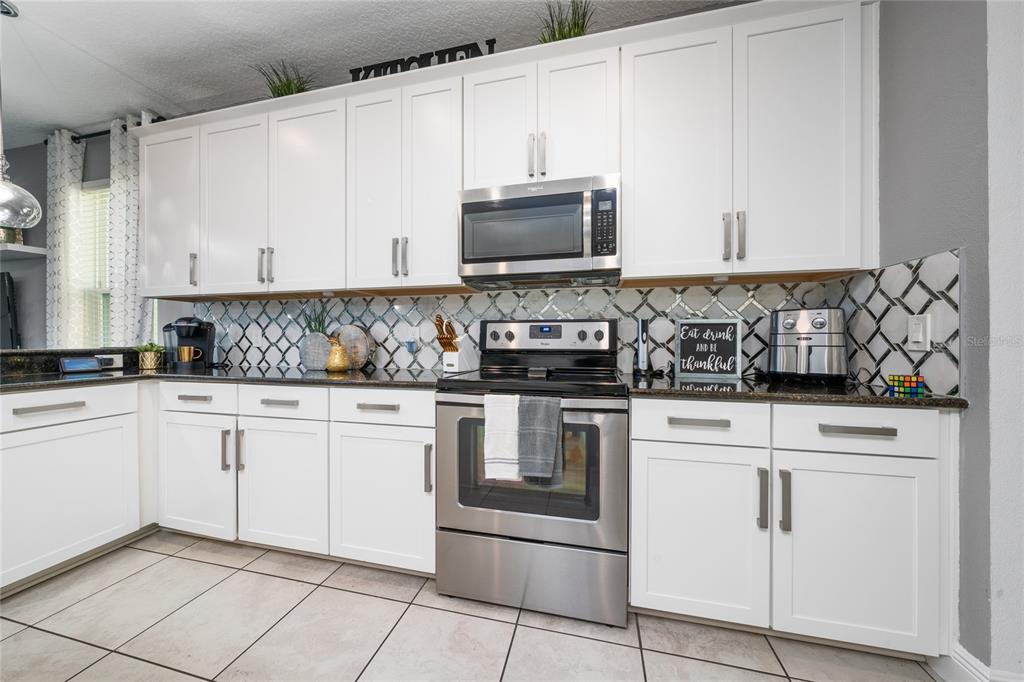 A kitchen features white cabinets, stainless steel appliances, dark countertops, and a patterned tile backsplash — 3243 PALATKA STREET, ORLANDO, FL