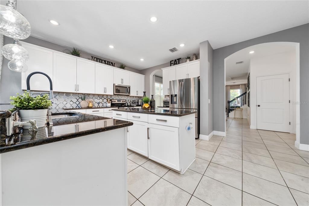 A kitchen features white cabinetry, a dark granite island, and light tile flooring — 3243 PALATKA STREET, ORLANDO, FL