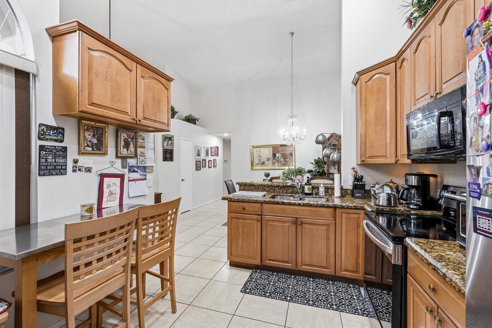 A kitchen with wood cabinets, granite countertops, stainless steel appliances, and a small dining area — 10933 Stafford Circle S, Boynton Beach FL 33436, BOYNTON BEACH, FL