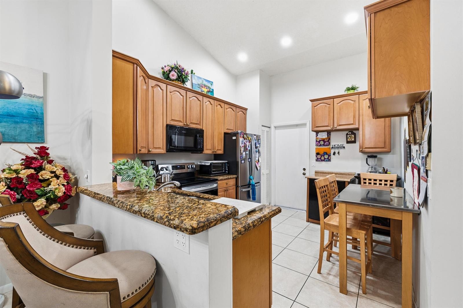 A kitchen with wood cabinets, granite countertops, a breakfast bar, and a small dining table — 10933 Stafford Circle S, Boynton Beach FL 33436, BOYNTON BEACH, FL