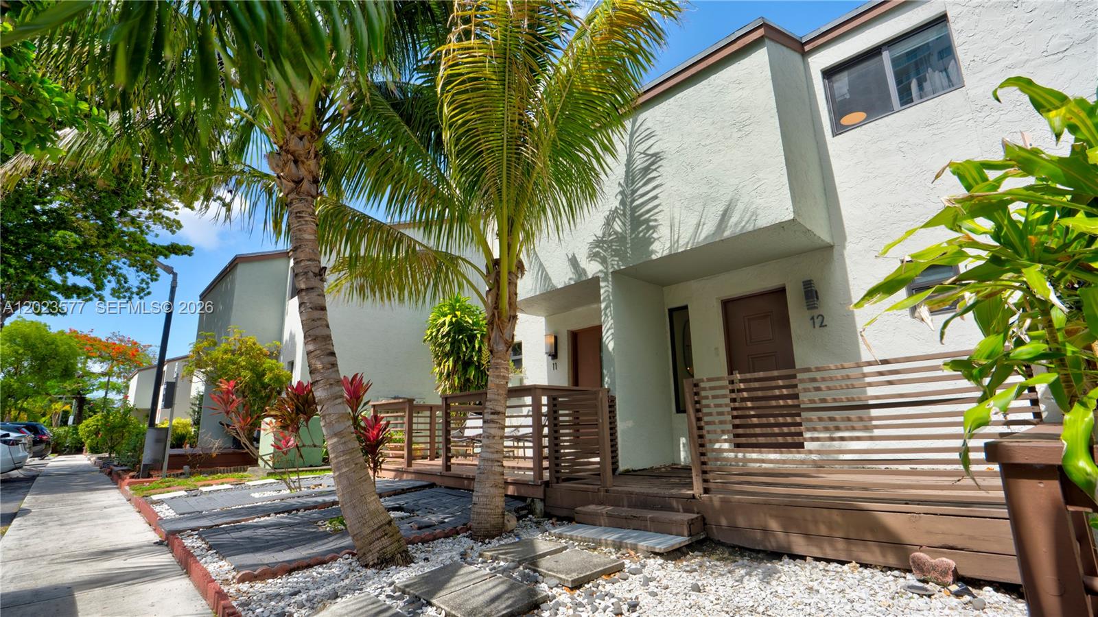 The exterior of a two-story townhouse features a wooden deck, palm trees, and gravel landscaping — 1901 NW S River Dr # 12B, Miami FL 33125, MIAMI, FL