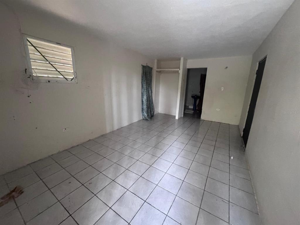 An empty room features white walls, light-colored floor tiles, a window, and a closet area — 62.2 KM. CARR#1 BO PEDRO DAVILA, CAYEY, PR
