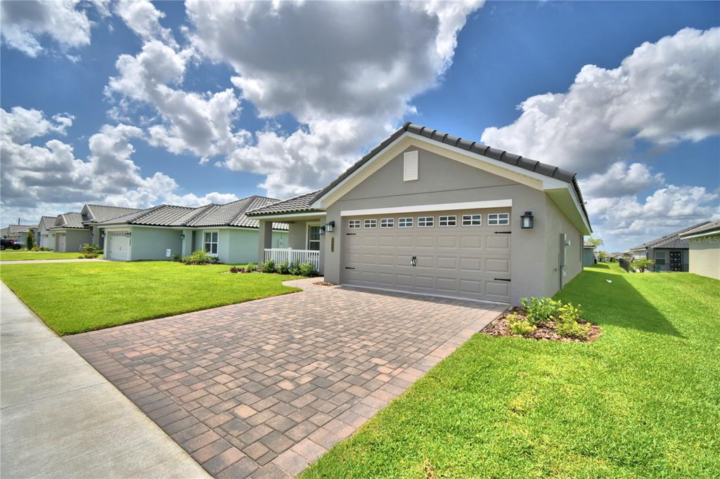 A gray single-story house with a paved driveway and a two-car garage under a cloudy sky — 4663 GRANDVIEW GLEN DRIVE, AUBURNDALE, FL