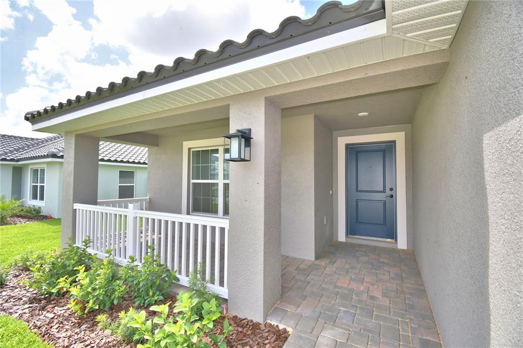 A covered front porch with a blue door, white railing, and paver flooring — 4663 GRANDVIEW GLEN DRIVE, AUBURNDALE, FL