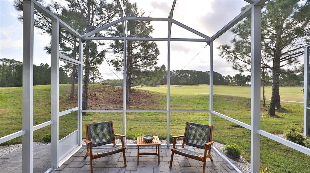 A screened-in patio with two chairs and a small table overlooks a grassy golf course — 3058 ISLES WAY, NEW SMYRNA BEACH, FL