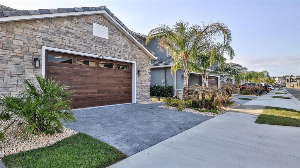 A stone-faced house with a wooden garage door and a paved driveway sits on a street — 3058 ISLES WAY, NEW SMYRNA BEACH, FL