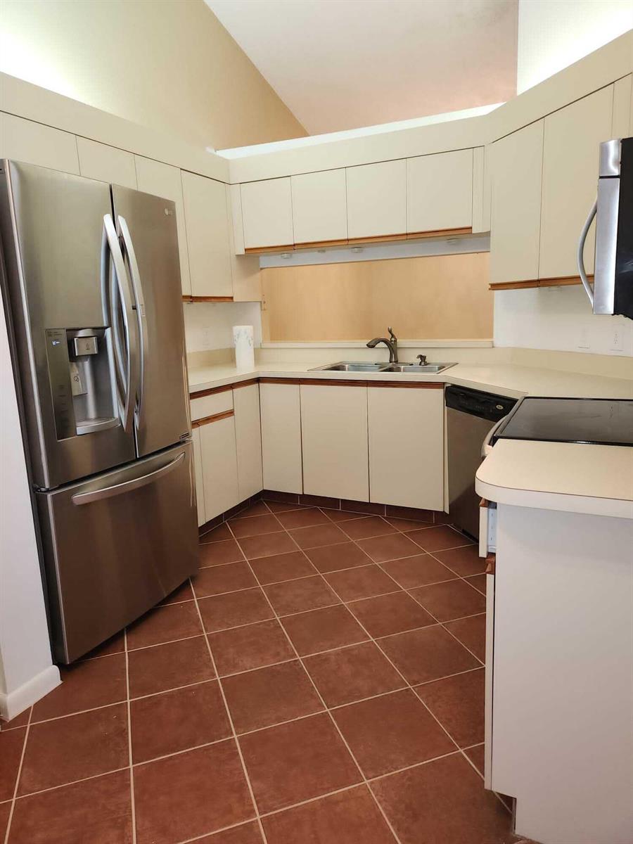 A kitchen with stainless steel appliances, off-white cabinets, light countertops, and reddish-brown tile flooring — 6531 SE Federal Highway # F211, Stuart FL 34997, STUART, FL