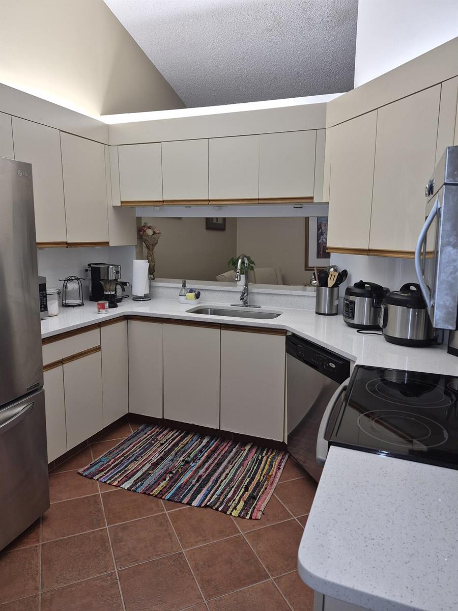 A kitchen features white flat-panel cabinets, stainless steel appliances, quartz countertops, and terracotta tile flooring — 6531 SE Federal Highway # F211, Stuart FL 34997, STUART, FL