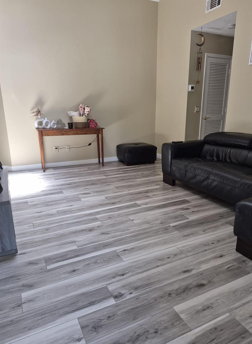 A living room features light gray wood-look flooring, beige walls, and a black leather sofa — 6531 SE Federal Highway # F211, Stuart FL 34997, STUART, FL
