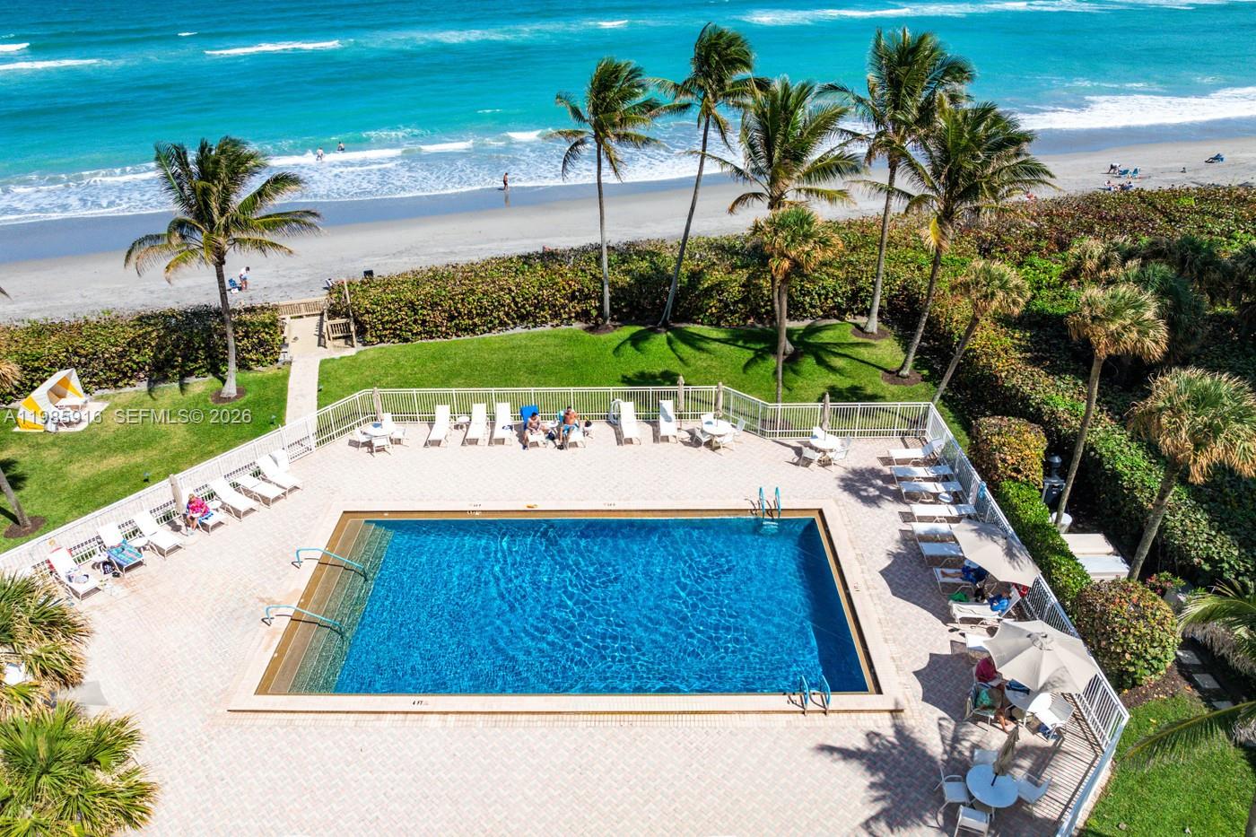 An aerial view shows a rectangular swimming pool surrounded by lounge chairs and palm trees — 500 Ocean Dr # 12A, Juno Beach FL 33408, JUNO BEACH, FL