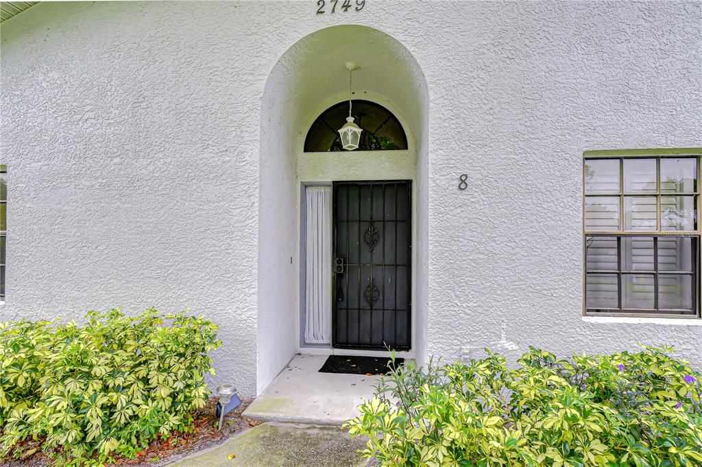 A front entrance with a black security door, arched transom window, and surrounding landscaping — 2749 COUNTRYSIDE BOULEVARD UNIT 8, CLEARWATER, FL