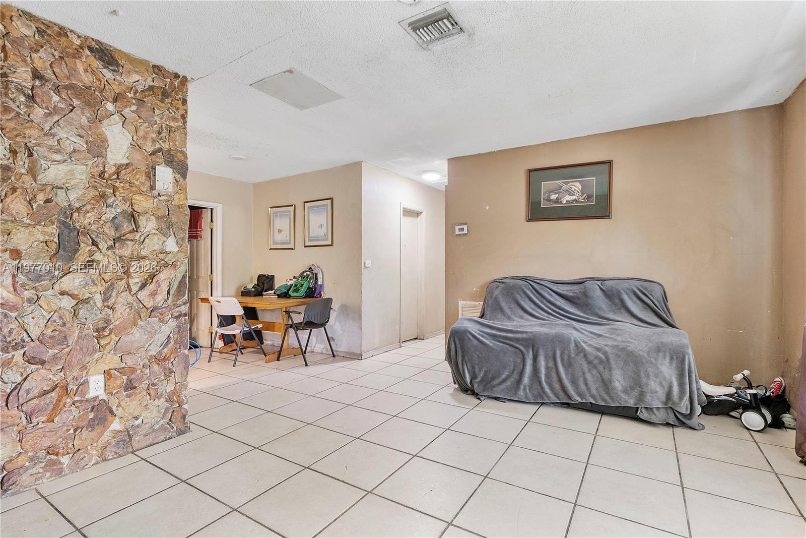 A living room features a stone accent wall, tiled floors, and a couch with a cover — 800 NW 33rd Ave, Lauderhill FL 33311, LAUDERHILL, FL