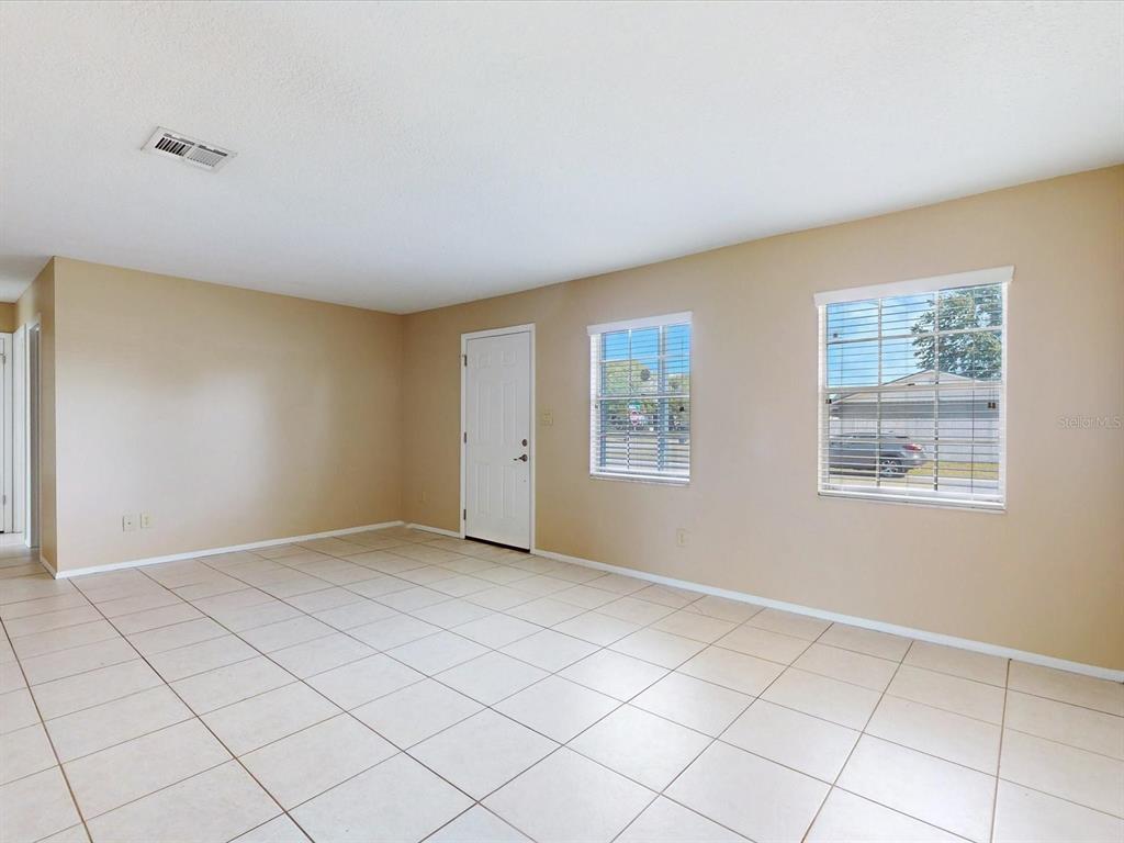 An empty room with beige walls, light-colored tile flooring, two windows, and a white door — 98 PINATA COURT, KISSIMMEE, FL