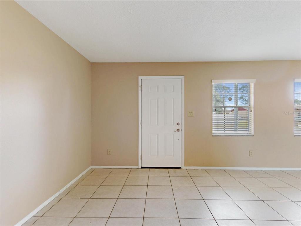 A room with beige walls, tiled flooring, a white front door, and a window — 98 PINATA COURT, KISSIMMEE, FL