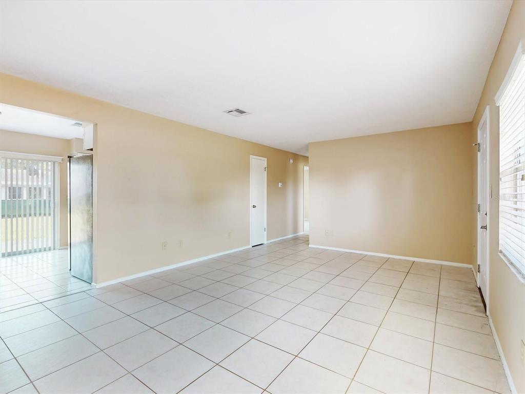 An empty room with beige walls, white tile flooring, and a sliding glass door — 98 PINATA COURT, KISSIMMEE, FL