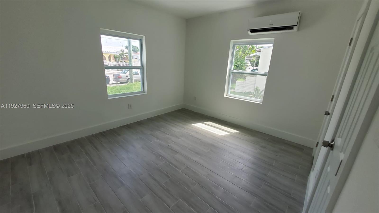 A bedroom features white walls, gray wood-look tile flooring, two windows, and a wall-mounted air conditioner — 560 NW 53rd St, Miami FL 33127, MIAMI, FL