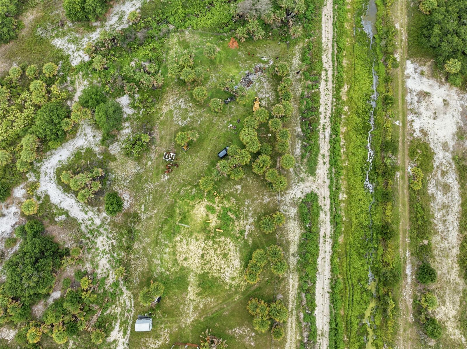 Aerial view of a rural property with scattered trees, a dirt road, and a small trailer — 19998 NW 270th Street, Okeechobee FL 34972, OKEECHOBEE, FL
