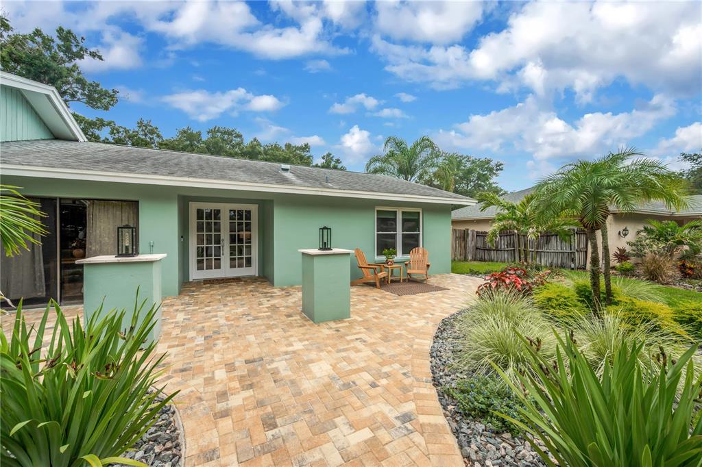 A light green house exterior features a paved patio, French doors, and landscaped garden beds — 2767 WESTCHESTER DRIVE N, CLEARWATER, FL