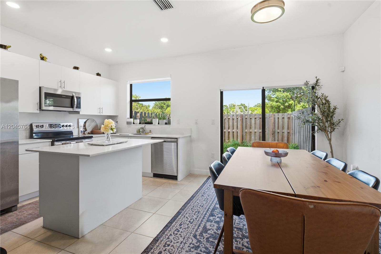 A modern kitchen with white cabinets and an island opens to a dining area — 23101 SW 99th Ave, Cutler Bay FL 33190, CUTLER BAY, FL