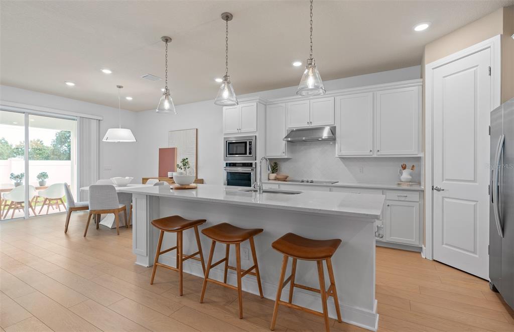 A modern kitchen features white cabinetry, a quartz island with bar stools, and light flooring — 4806 FINLEY DRIVE, DAVENPORT, FL