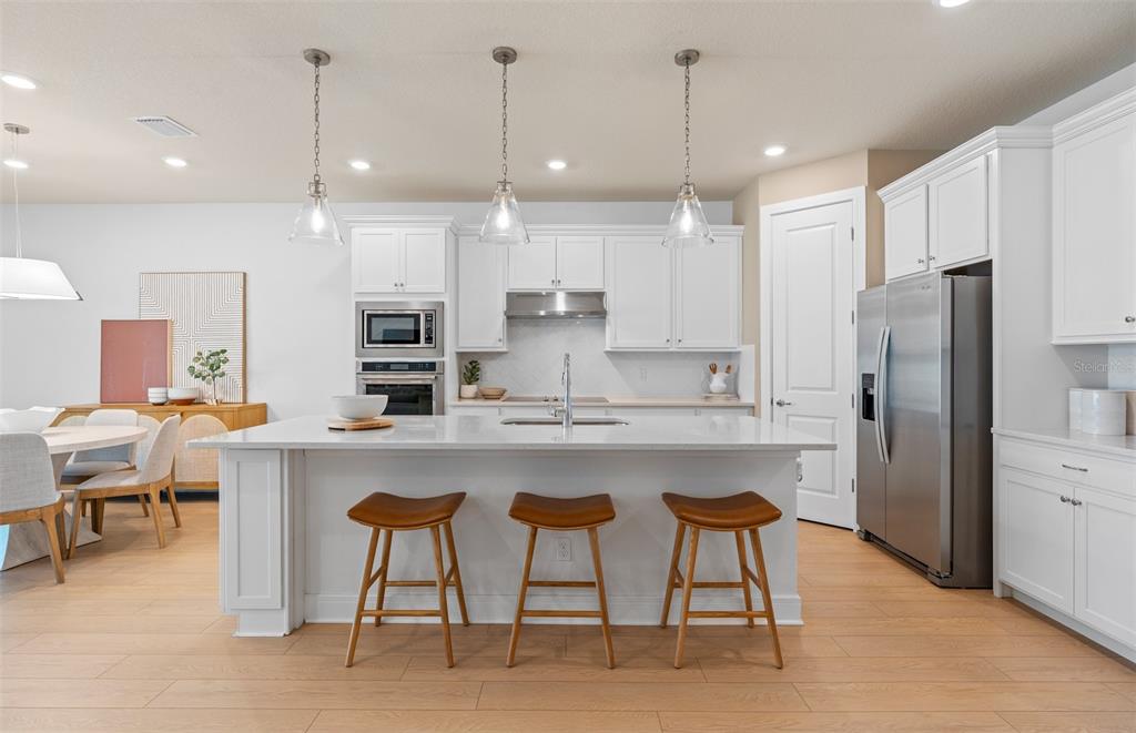 A modern kitchen features white cabinetry, a large island with three stools, and stainless appliances — 4806 FINLEY DRIVE, DAVENPORT, FL