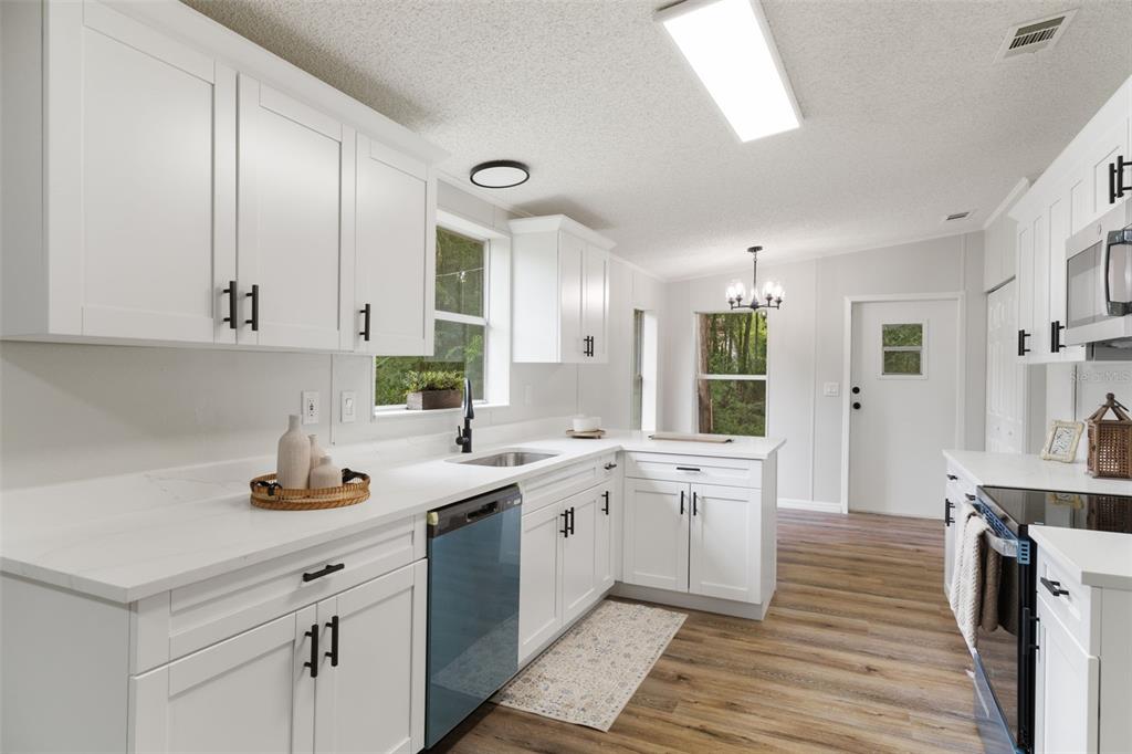 A bright kitchen features white cabinets, quartz countertops, stainless steel appliances, and wood-look flooring — 20645 STEWART ROAD, DADE CITY, FL