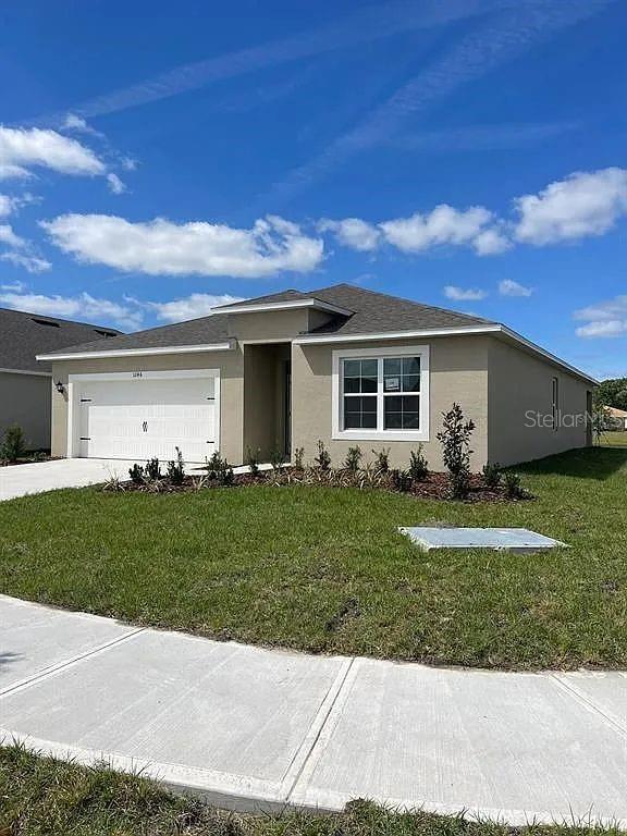 A single-story house with a tan exterior, a two-car garage, and a front lawn — 1246 RED HILL ROAD, DAVENPORT, FL