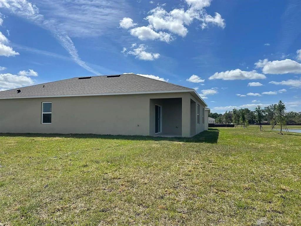The exterior rear view of a tan house features a covered patio and a grassy yard — 1246 RED HILL ROAD, DAVENPORT, FL