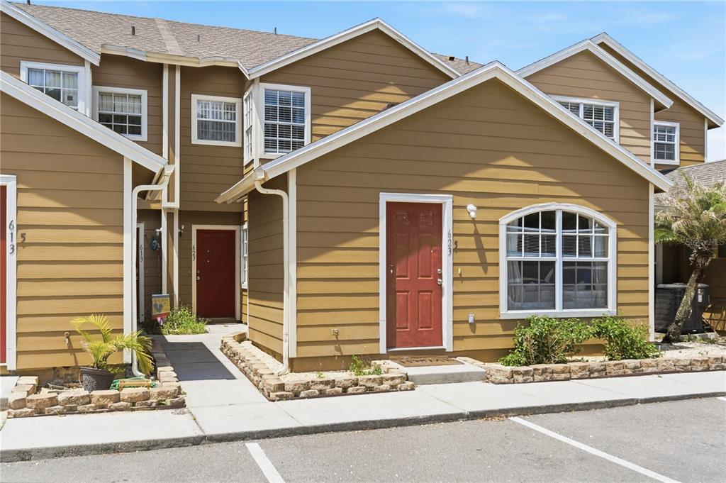 A tan two-story townhouse exterior features red front doors and a small stone garden bed — 623 COCONUT PALM WAY UNIT 0, DAVENPORT, FL