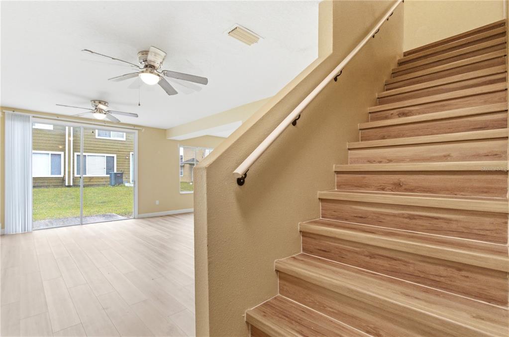 A staircase with wood-look treads leads up from a living area with sliding glass doors — 623 COCONUT PALM WAY UNIT 0, DAVENPORT, FL