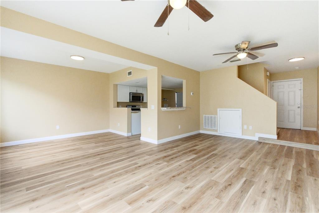 An open-concept living area features light wood-look flooring, beige walls, and a pass-through kitchen — 623 COCONUT PALM WAY UNIT 0, DAVENPORT, FL